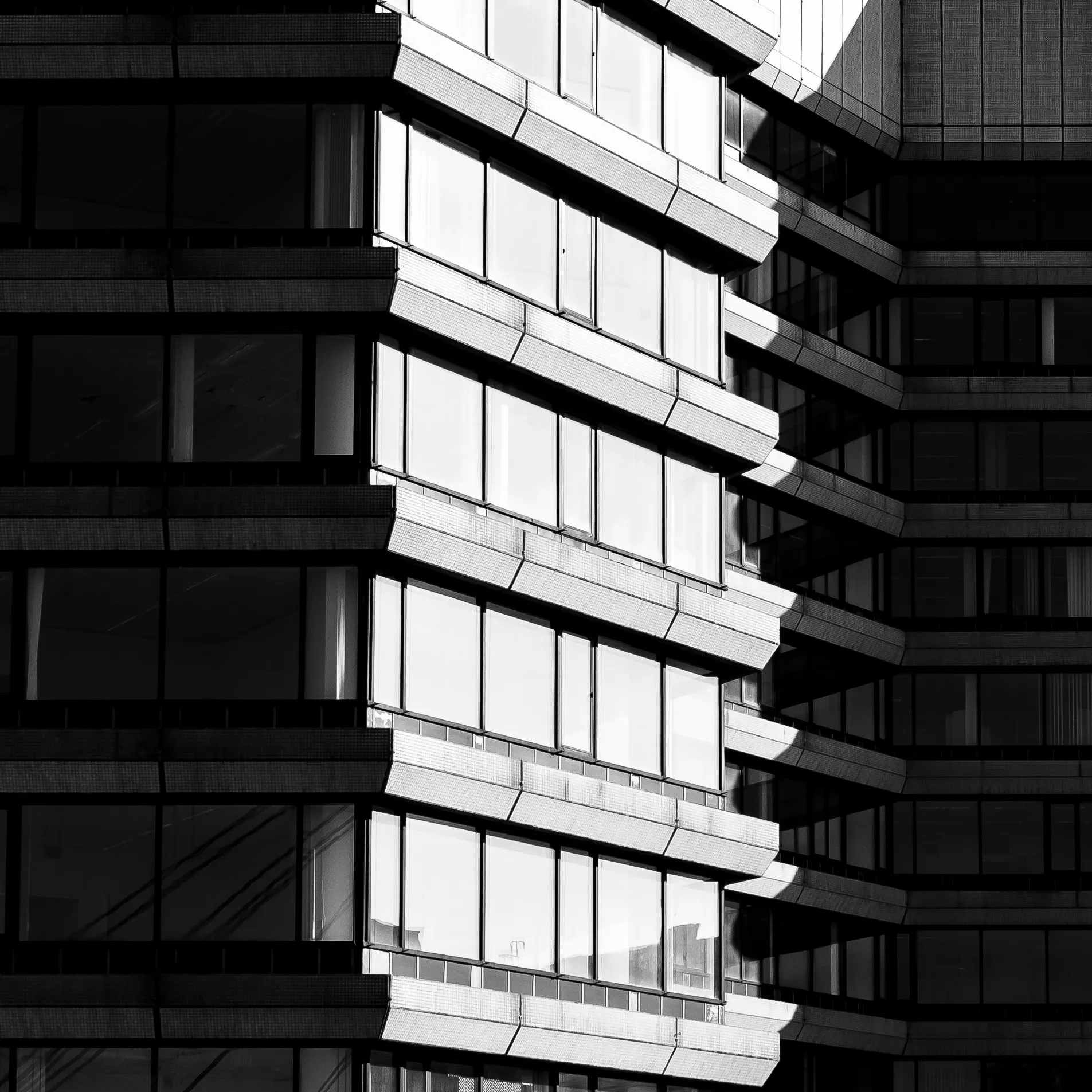A black and white photo of the side of a building brightly lit by sunlight. The side of the building is at an angle, such that the left and right thirds of the frame are significantly darker, covered by shadows.