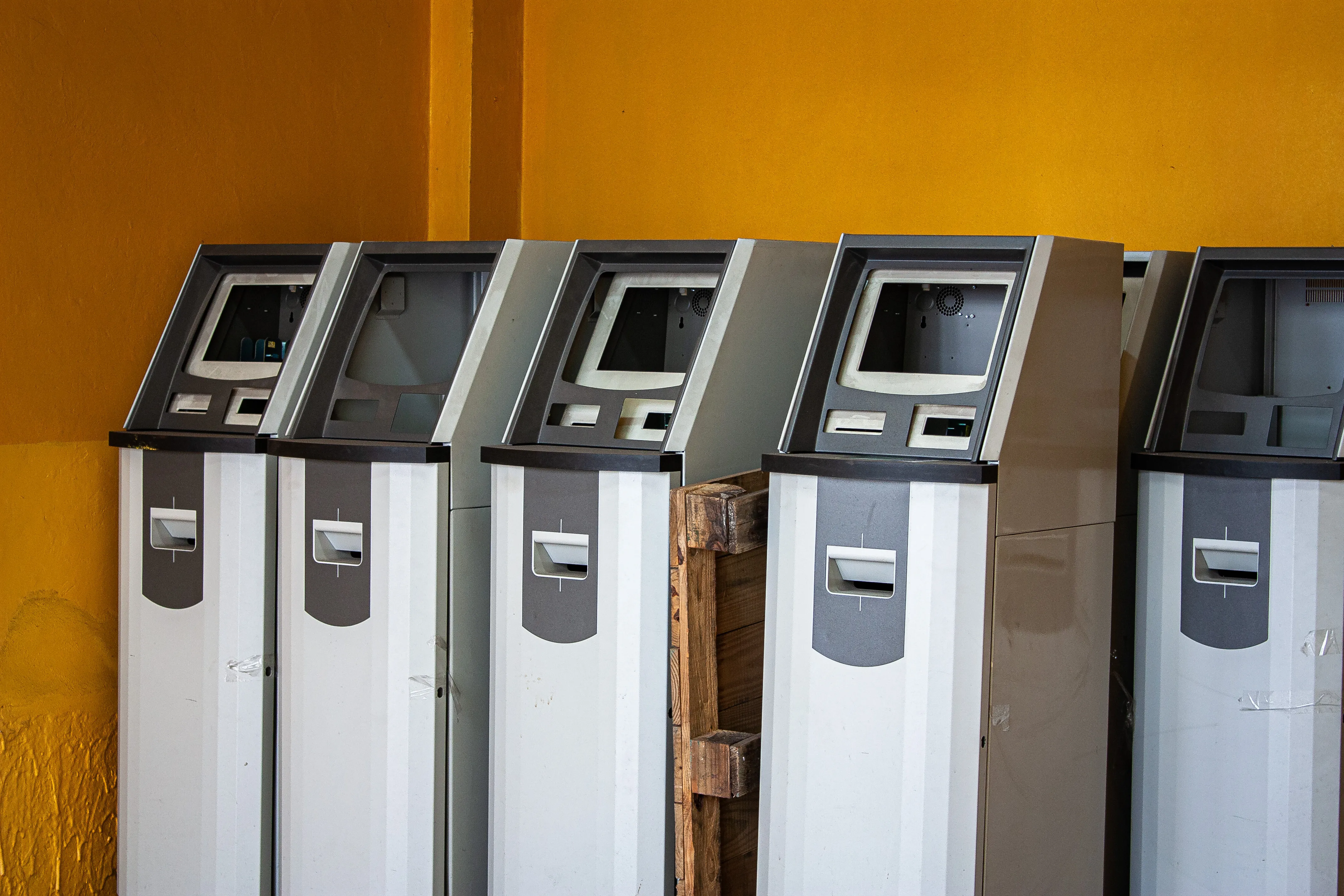 A photo of multiple empty bodies of what appear to be ATMs. All electronics have been removed, and the bodies lie standing next to eachother in the corner of a yellow room.