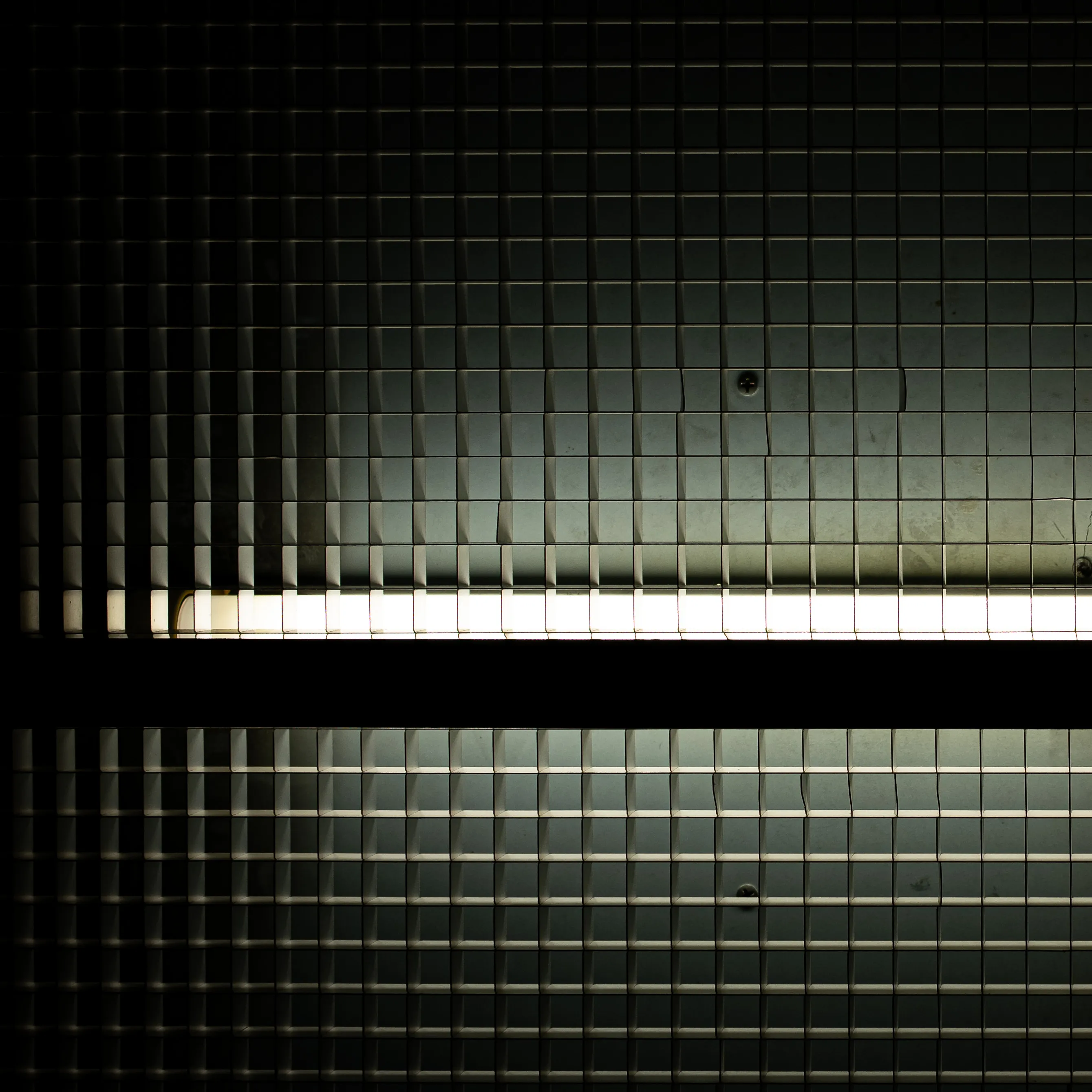 A grid of metal stripes, some of them slightly deformed, covering a single horizontal tube of fluorecent light.