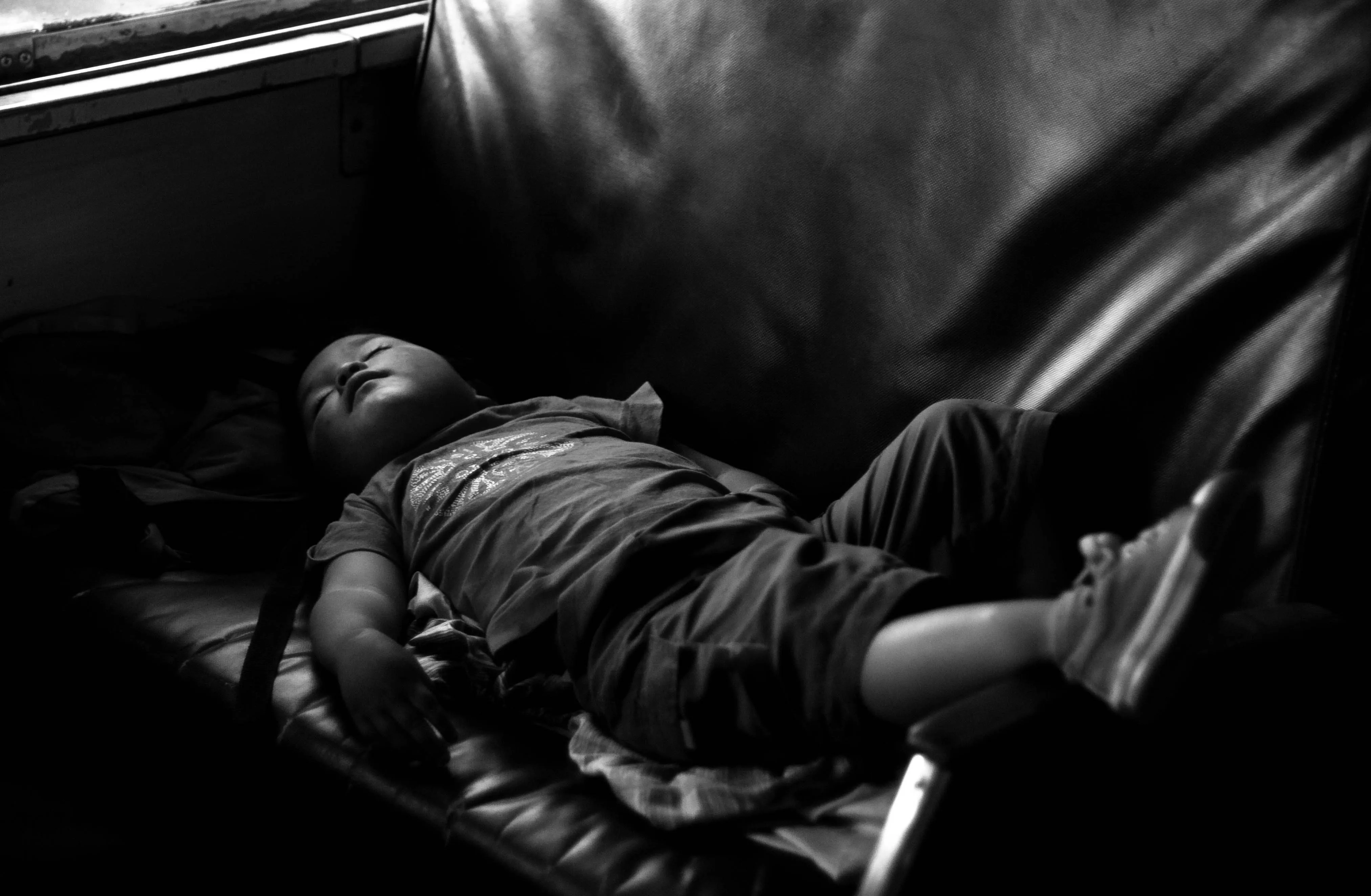 A child lies across the seat of a train, sleeping, with one leg up on the arm rest.